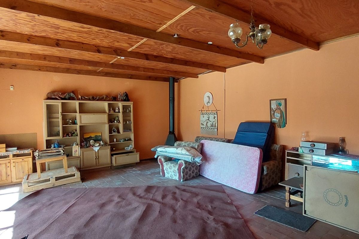 Spacious living room featuring exposed wooden ceiling beams, terracotta-style flooring, and a built-in fireplace, offering a rustic farm-style aesthetic.
