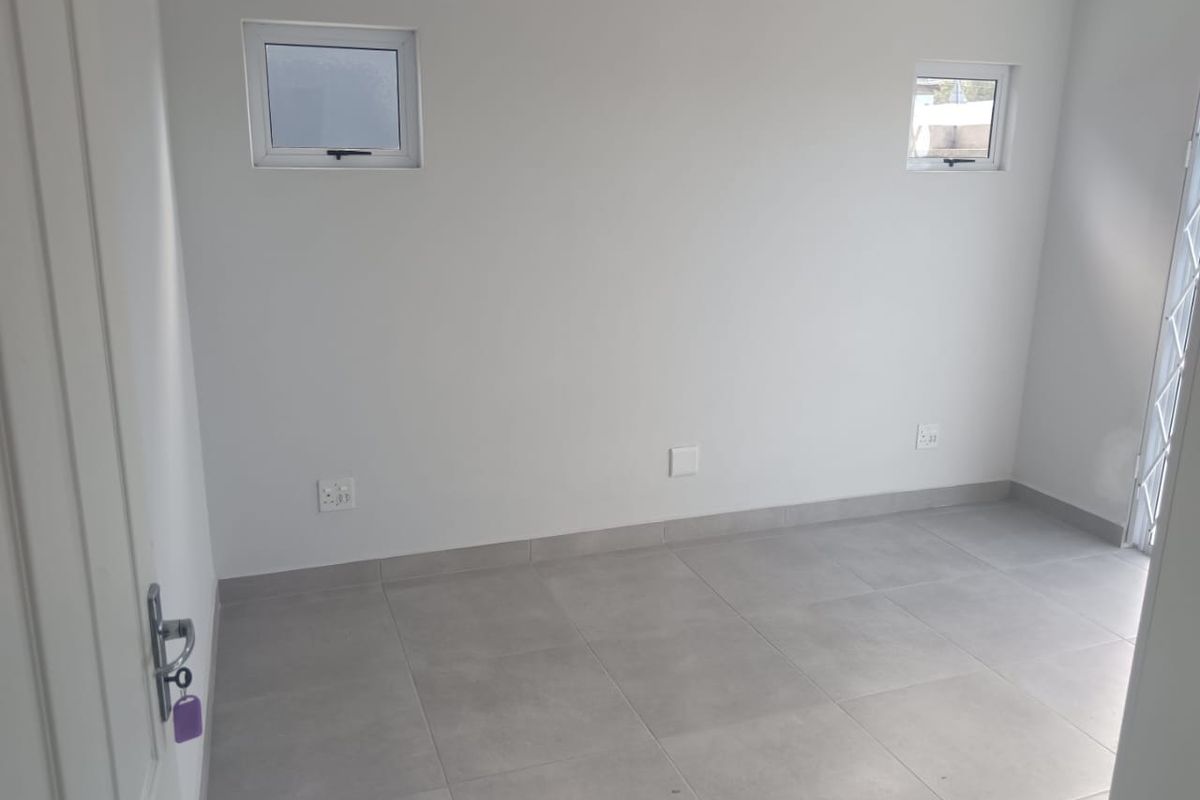 A clean, empty bedroom featuring neutral grey floor tiles, white walls, and two small high-set windows, providing a bright and versatile living space.