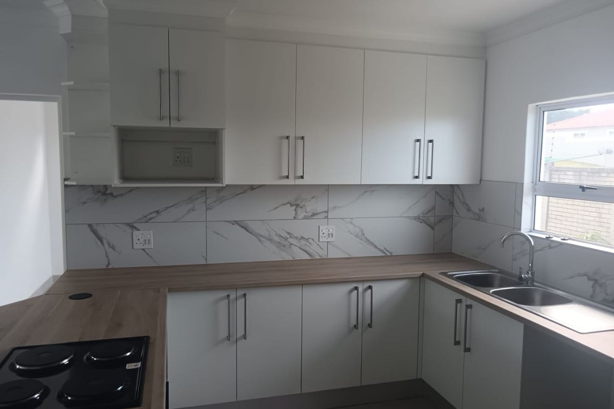 Modern kitchen featuring white cabinetry, wood-look countertops, marble-effect tiled backsplash, and a built-in electric hob.
