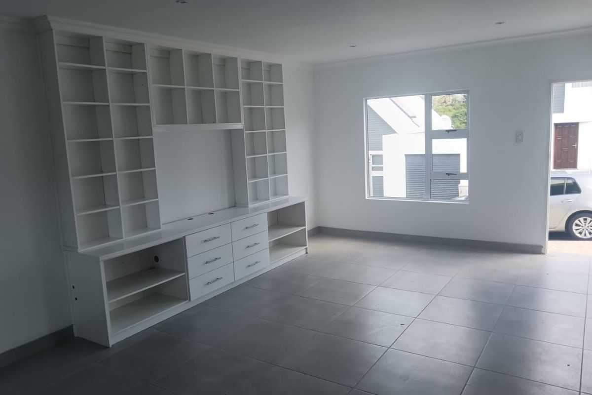A bright, open-plan living area featuring large-format floor tiles and a substantial built-in white cabinetry unit with integrated shelving and storage drawers.