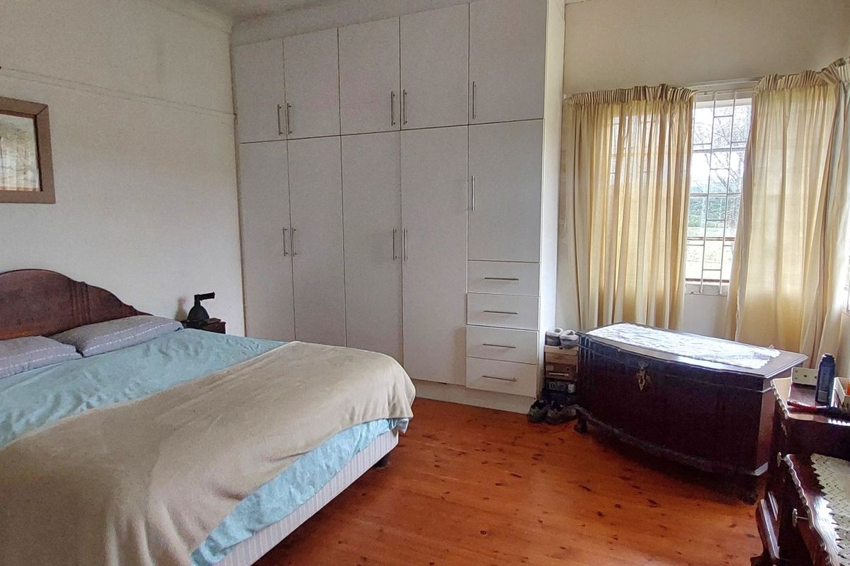 A spacious bedroom featuring polished timber flooring, built-in floor-to-ceiling cabinetry, and large windows with security bars.