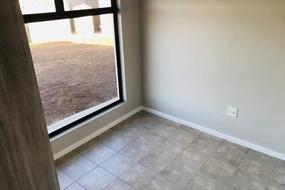 A bright, empty bedroom featuring neutral grey tiled flooring, modern black-framed windows, and clean, freshly painted walls.