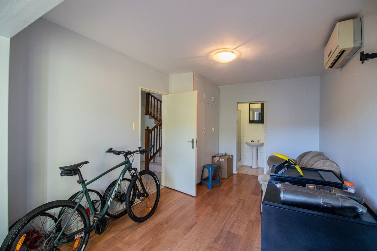A multi-purpose living space featuring laminate flooring, built-in storage cupboards, and an attached en-suite bathroom with a pedestal basin.