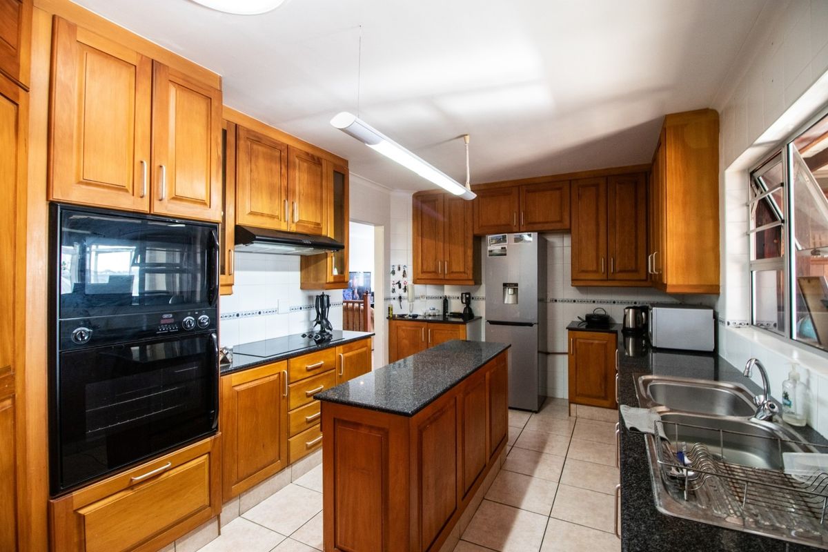 A functional kitchen featuring wooden cabinetry, granite countertops, a central island, and built-in oven and hob.