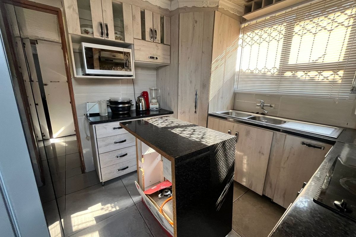 A functional kitchen featuring wood-look cabinetry, dark granite countertops, a central island, and a double stainless steel sink with natural light.