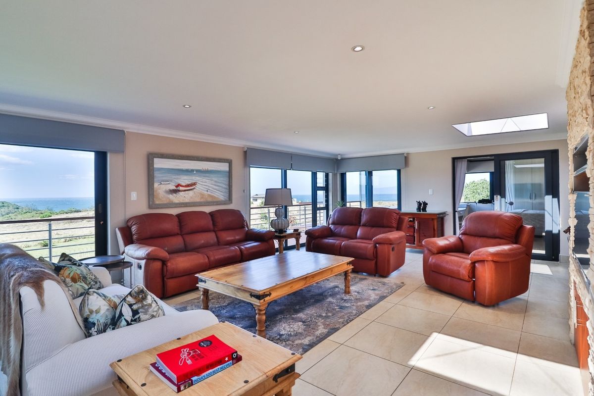 Spacious living room featuring large windows with ocean views, tiled flooring, recessed lighting, and a stone-clad feature wall.