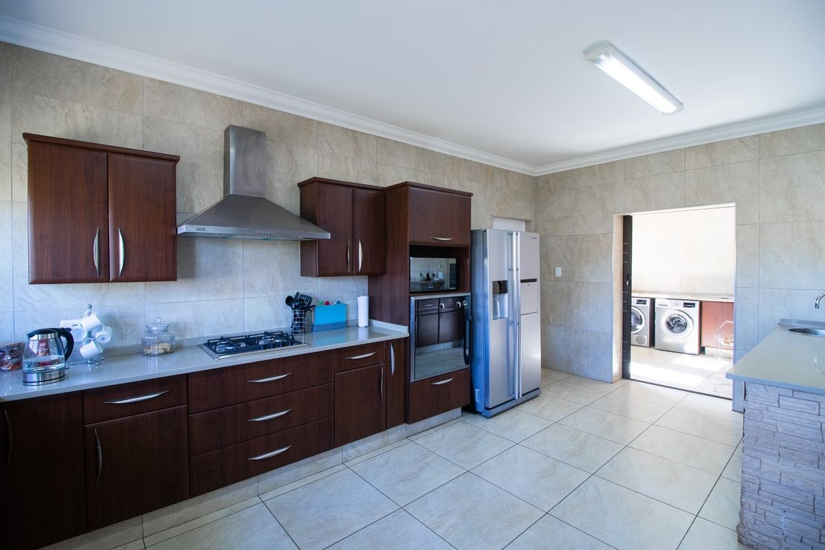 A functional kitchen featuring dark wood cabinetry, stone-look wall tiles, a built-in oven, gas hob, extractor fan, and an adjacent laundry area.