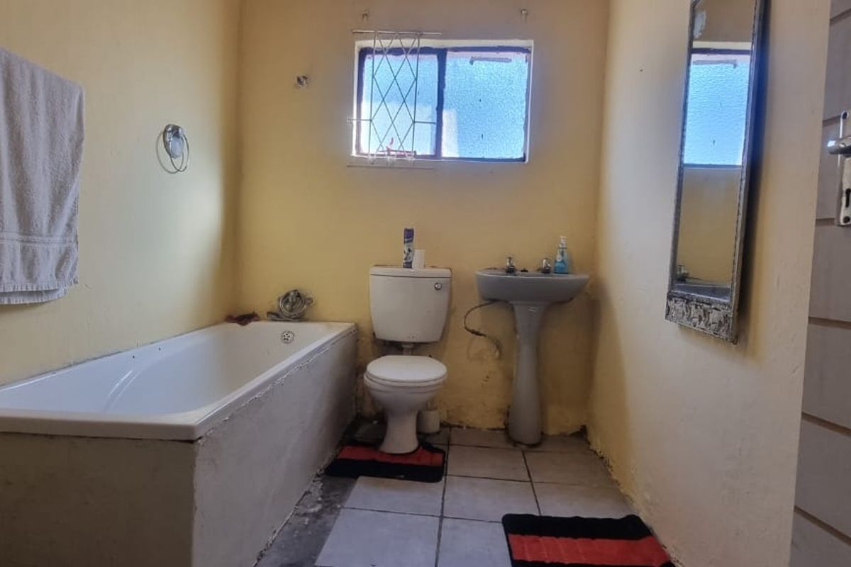 A dated bathroom featuring a standard bathtub, pedestal basin, and toilet, with tiled flooring and yellow wall finishes.