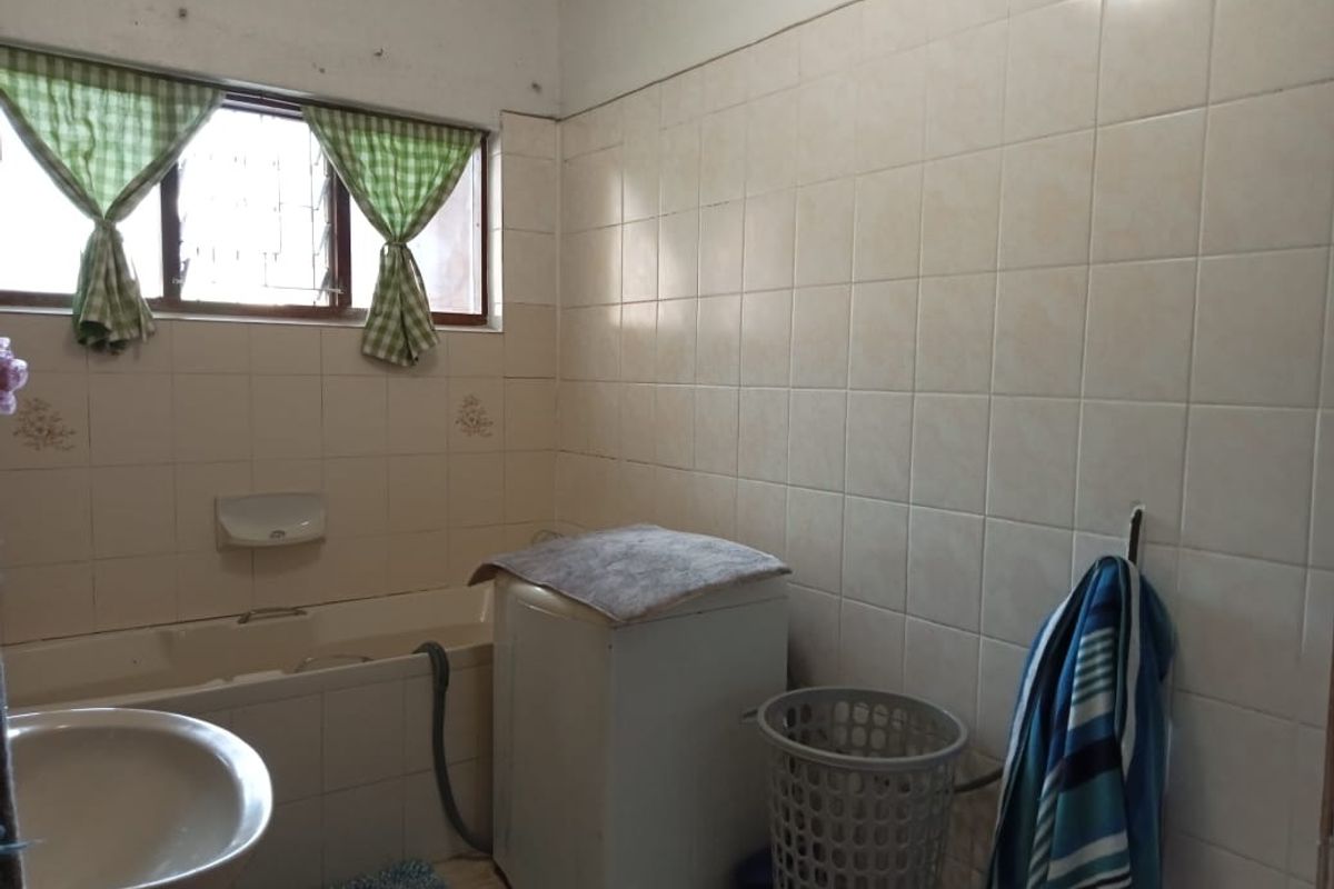 A dated bathroom featuring a built-in bathtub, wall-mounted basin, and full-height wall tiling, currently utilized with laundry facilities.