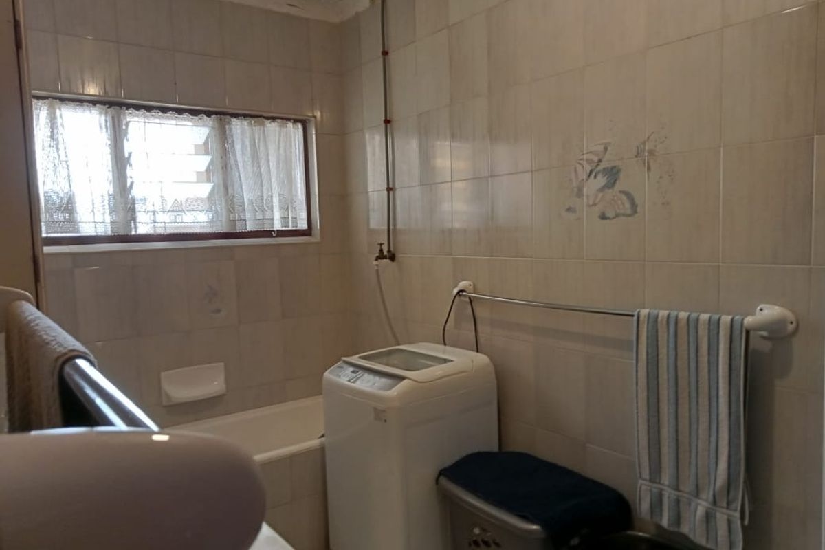 A functional bathroom featuring full-height wall tiling, a built-in bathtub, and a dedicated space for laundry appliances.