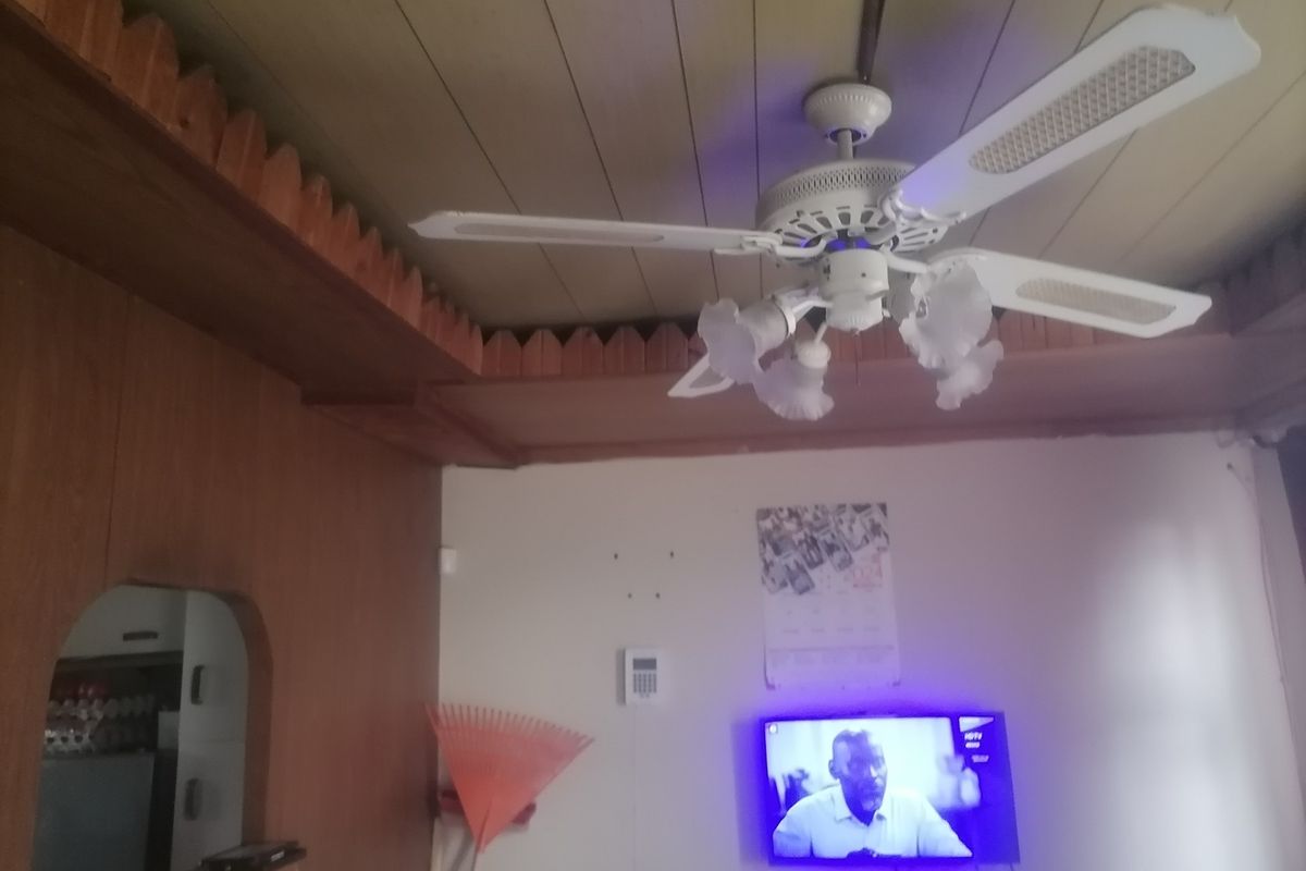 A living area featuring dated wood paneling, a ceiling fan with integrated lighting, and a wall-mounted security alarm keypad.