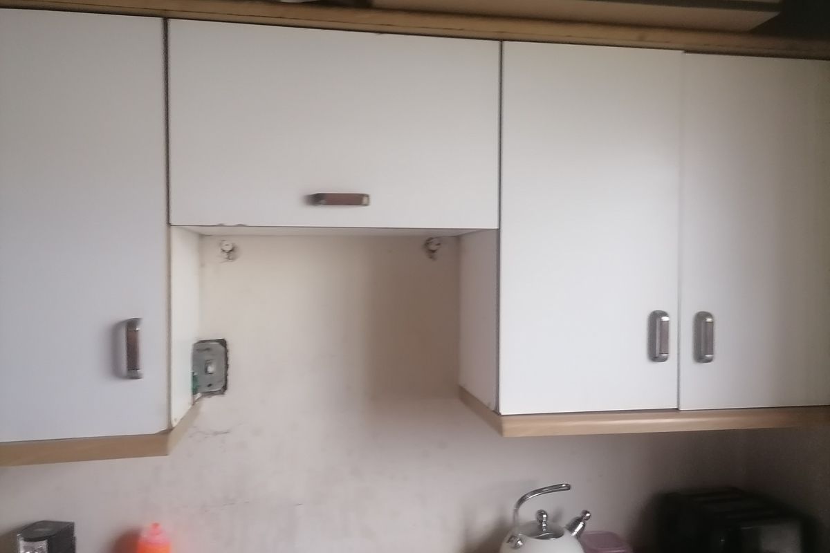 A kitchen area featuring white wall-mounted cabinetry with visible wear, an exposed electrical outlet, and a stained backsplash area.
