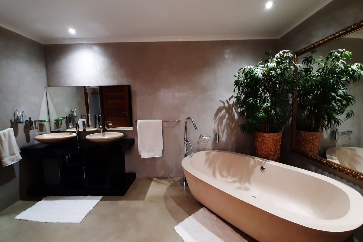 Modern bathroom featuring a freestanding bathtub, double vanity with vessel sinks, polished concrete floors, and contemporary cementitious wall finishes.