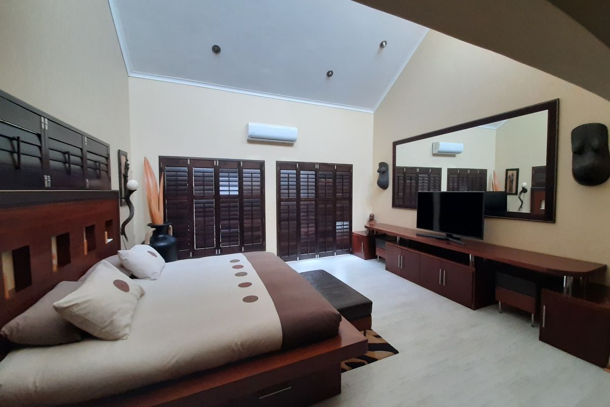 Spacious bedroom featuring a high vaulted ceiling, timber plantation shutters, and a wall-mounted split-system air conditioner.