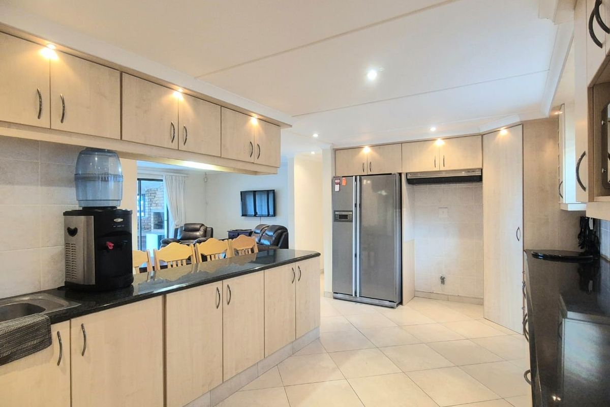 A spacious kitchen featuring light wood cabinetry, dark granite countertops, tiled flooring, and recessed lighting, with an open-plan layout flowing into the living area.