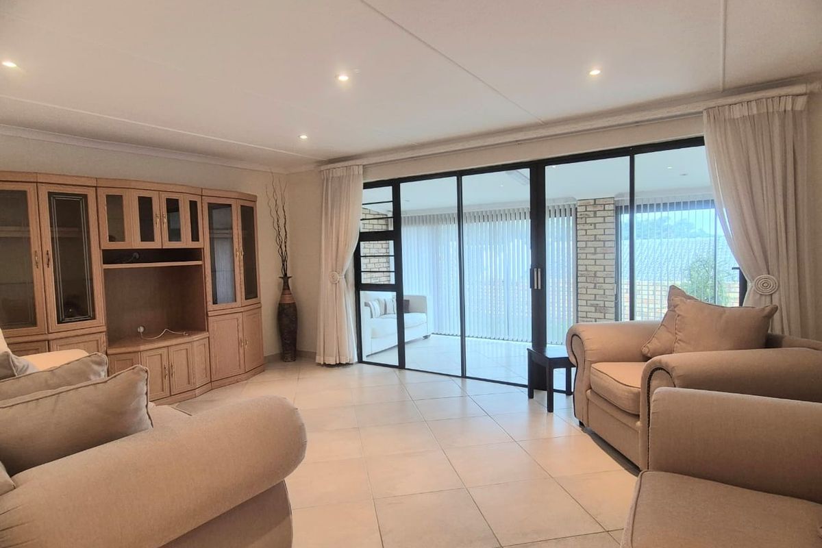Spacious living room featuring large sliding glass doors that open onto a covered patio, tiled flooring, and recessed ceiling lighting.