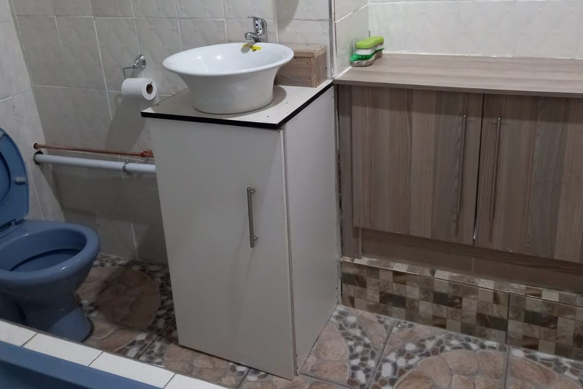 A functional bathroom featuring a vessel sink vanity, wood-look cabinetry, and tiled flooring. The space includes a toilet and wall-mounted plumbing fixtures.