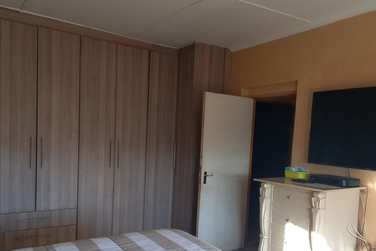 A bedroom featuring extensive built-in wooden cabinetry providing ample storage space, with a neutral wall finish and direct access to an adjoining room.