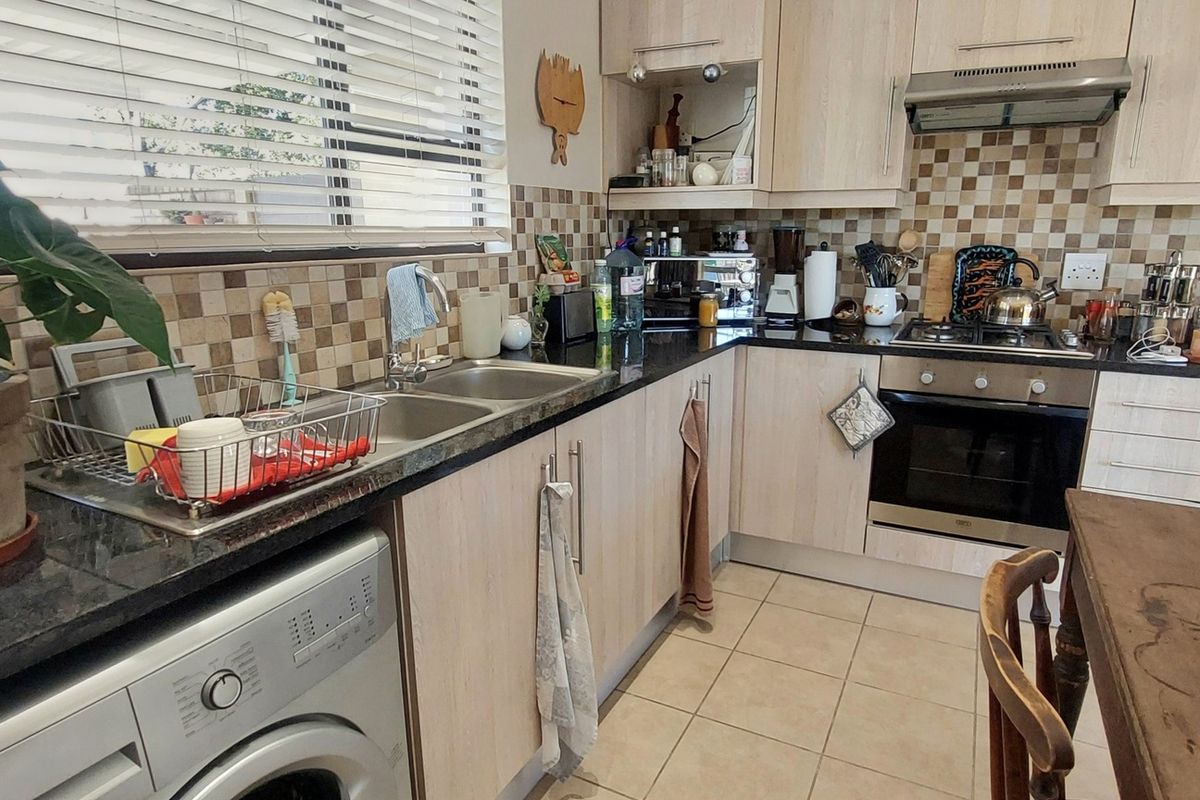 Functional kitchen featuring light wood-finish cabinetry, dark granite countertops, a built-in oven, extractor fan, and tiled splashback with integrated laundry plumbing.