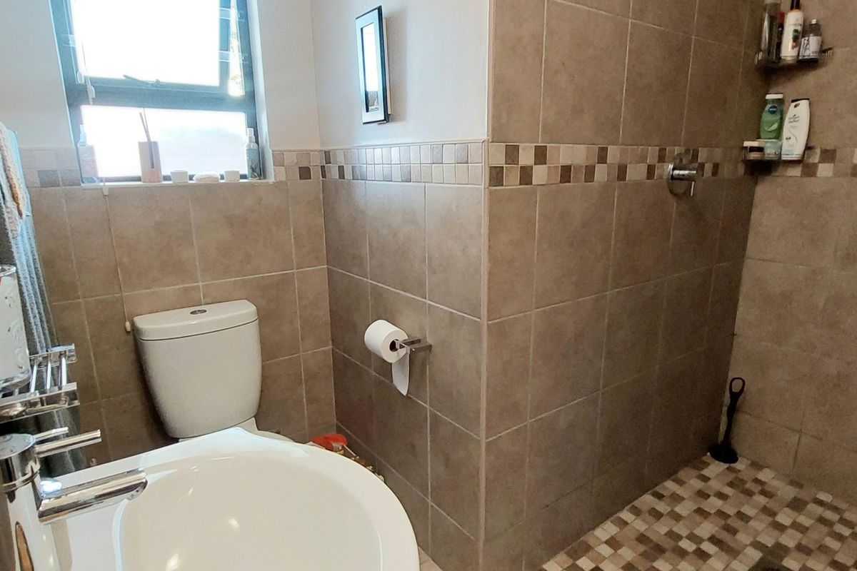 A functional bathroom featuring a walk-in shower with tiled walls, a pedestal basin, and a toilet, finished with neutral ceramic wall and floor tiles.