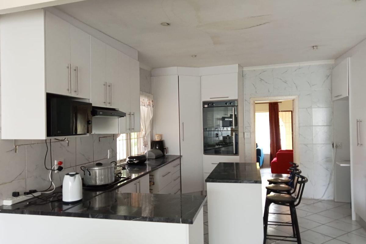 A functional kitchen featuring white cabinetry, dark stone countertops, a built-in oven, and a breakfast bar island, with an open-plan layout.