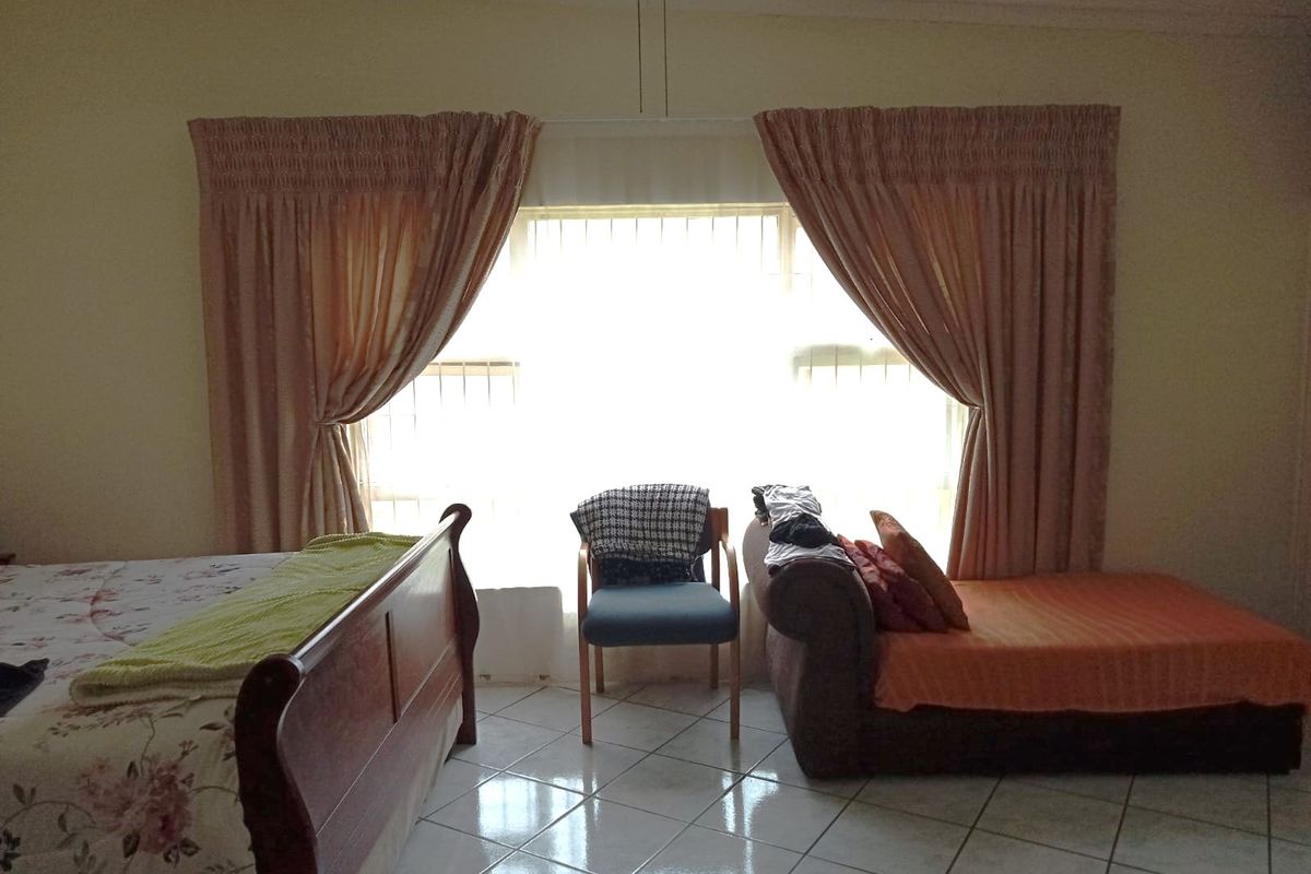 A bedroom featuring tiled flooring and a large window with curtains, providing natural light to the space.