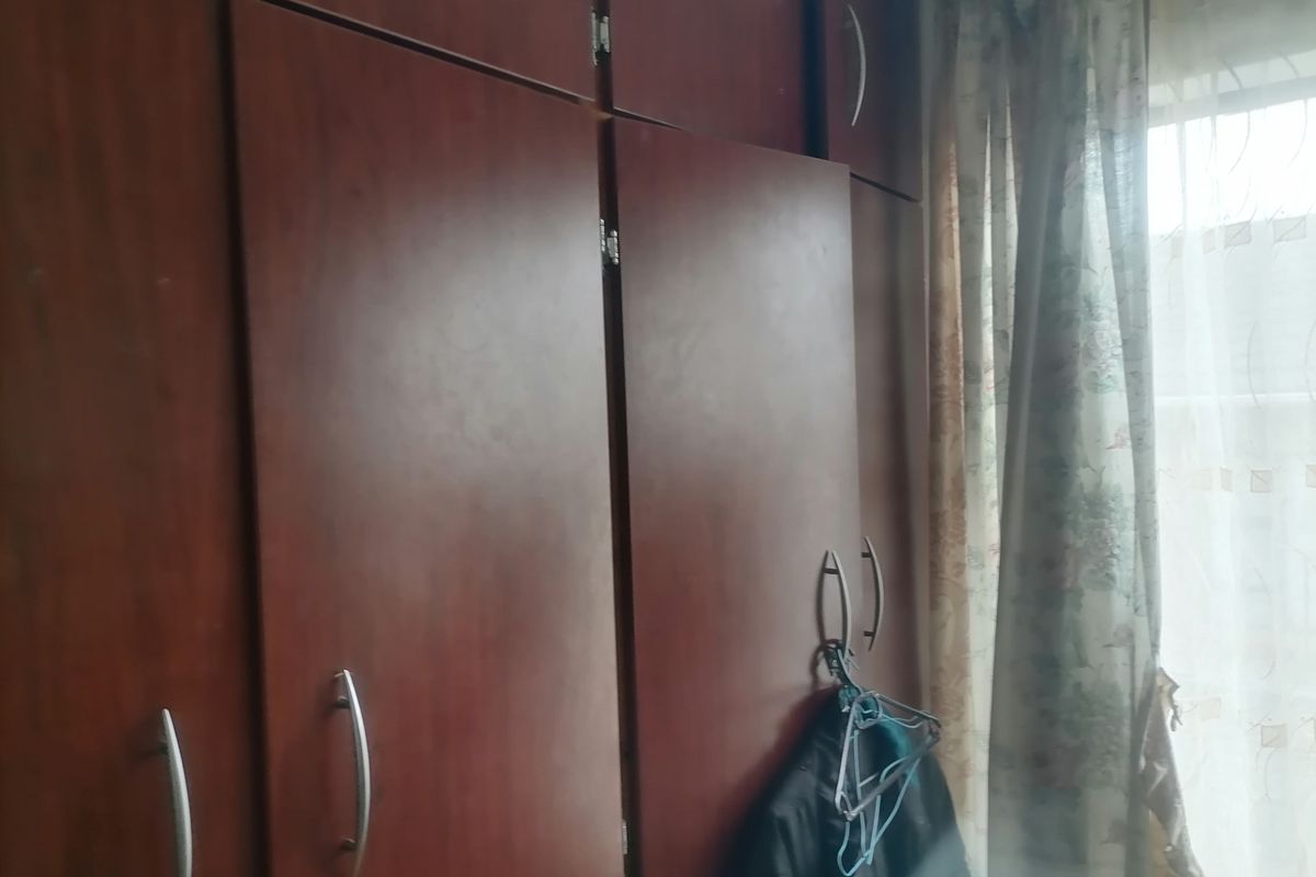 A bedroom featuring built-in wooden cabinetry with integrated storage and a window with curtains.