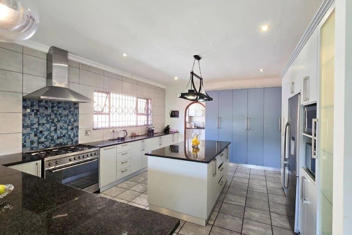 Modern kitchen featuring a central island, granite countertops, stainless steel gas stove with extractor fan, and ample built-in cabinetry.