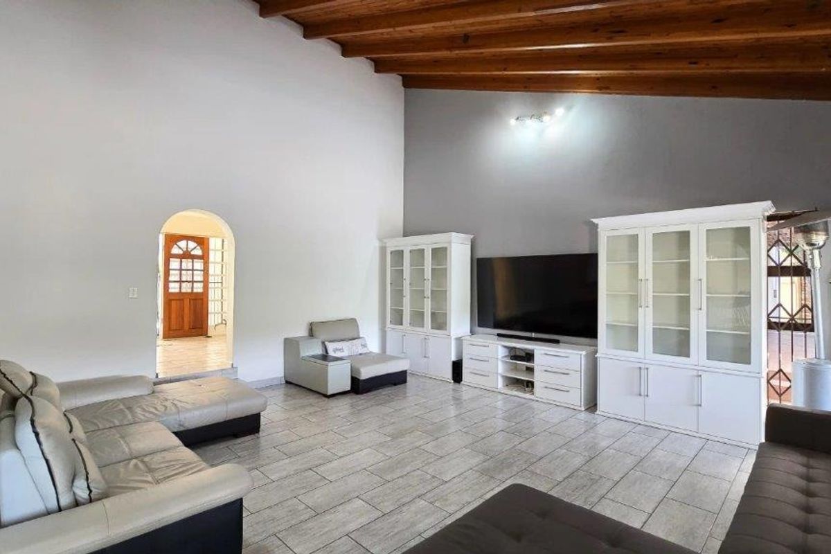 Spacious living room featuring high vaulted timber-beamed ceilings, tiled flooring, and an arched doorway leading to the entrance.