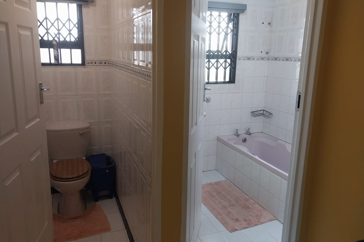 A functional bathroom layout featuring a separate toilet area and a tiled bathroom with a built-in bathtub and security-grilled windows.