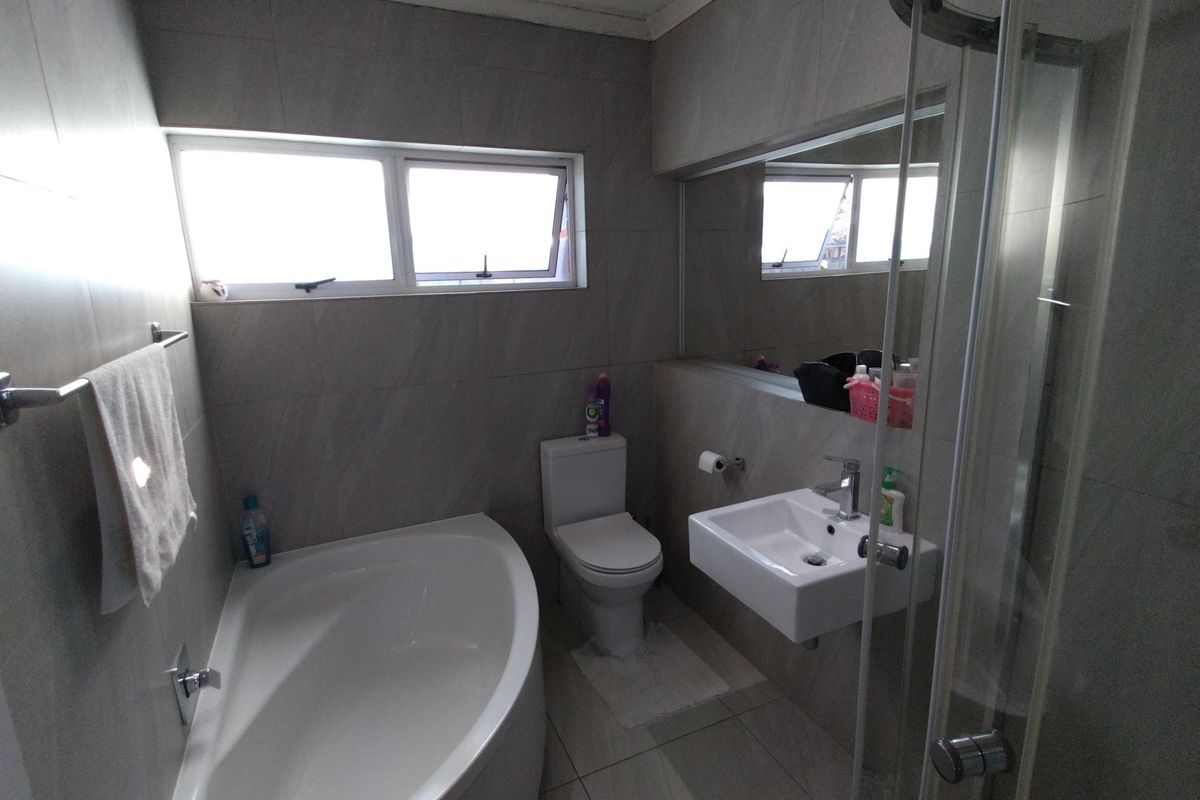 Modern bathroom featuring a corner bathtub, wall-mounted basin, toilet, and a glass-enclosed shower, finished with neutral floor-to-ceiling wall tiles.