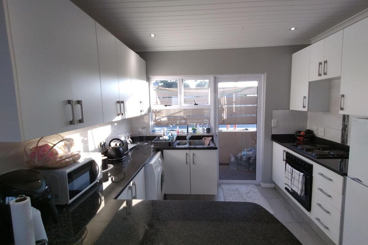 Modern kitchen featuring white cabinetry, dark granite countertops, integrated oven, and a glass door leading to an outdoor balcony area.