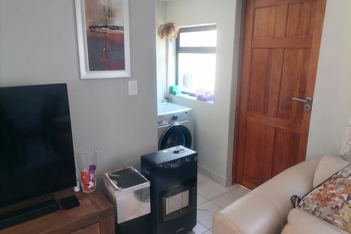 A view of a living area featuring a tiled floor, a wooden door, and a recessed laundry nook with a washing machine connection.