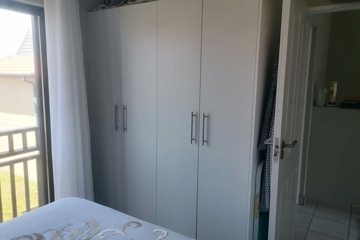 A bedroom featuring built-in white cabinetry with modern handles and access to a balcony through a sliding glass door.