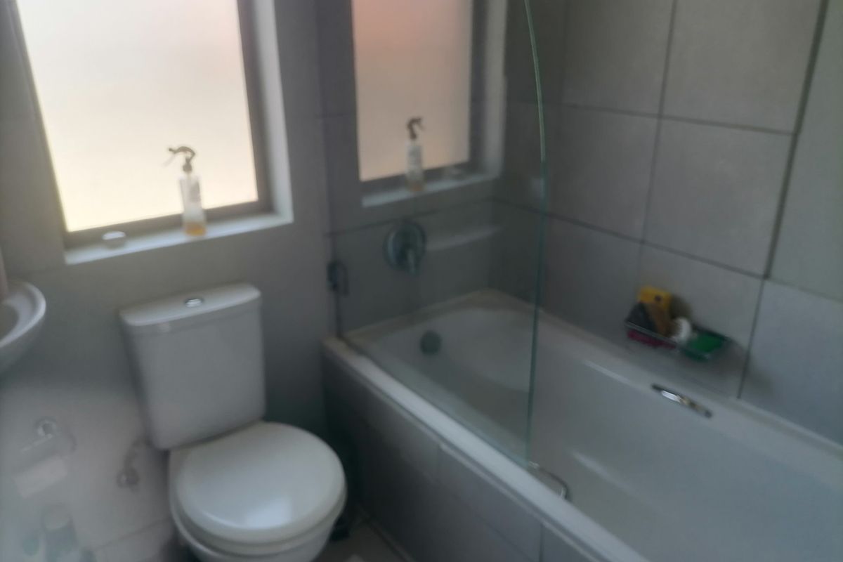 A functional bathroom featuring a bathtub with a glass shower screen, a toilet, and tiled walls.