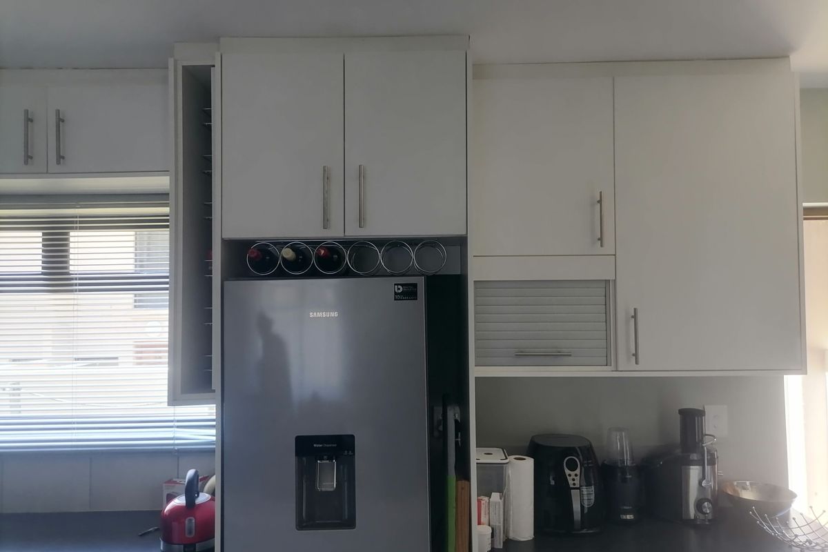 A functional kitchen area featuring white cabinetry, dark countertops, and a dedicated space for a refrigerator with integrated wine storage.