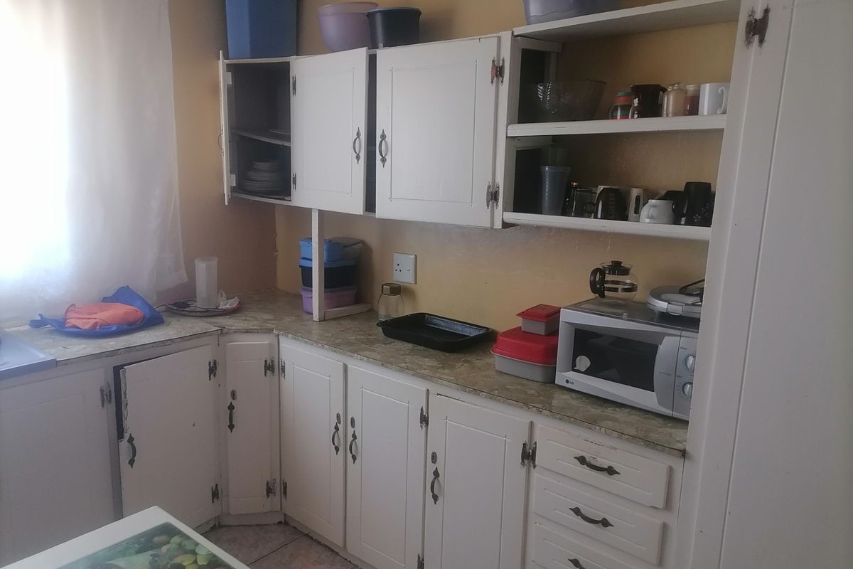 A functional kitchen featuring white cabinetry, laminate countertops, and open shelving, providing essential storage and workspace in a compact layout.