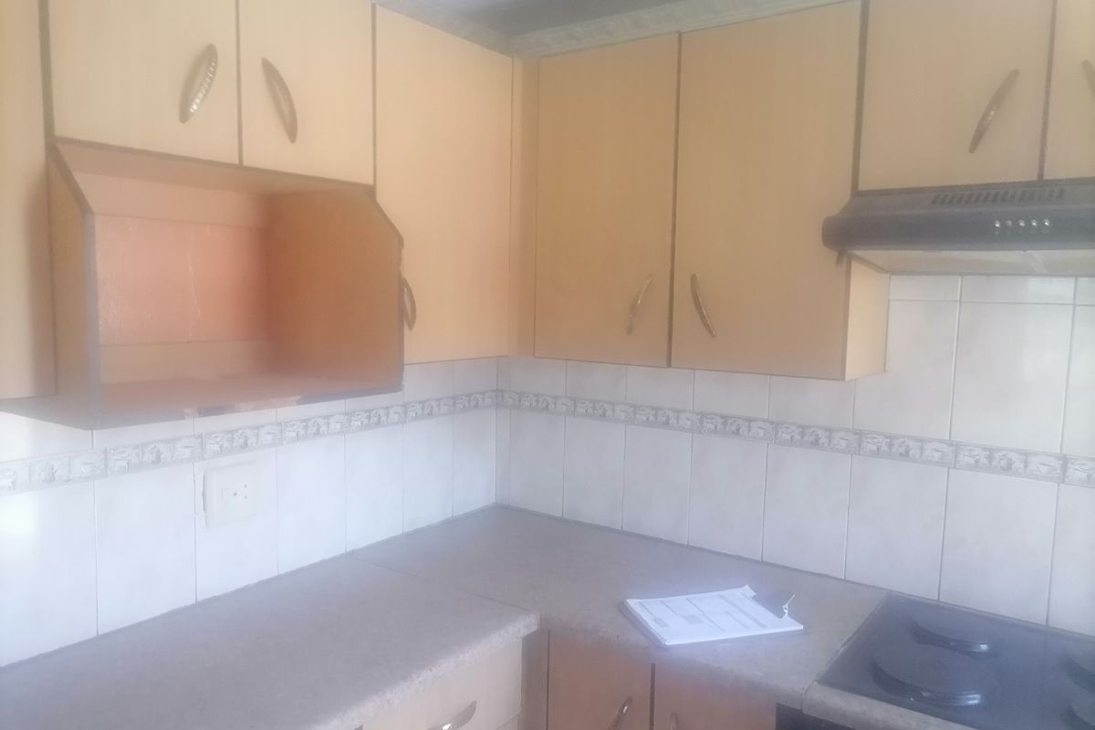 A dated kitchen featuring laminate countertops, tiled backsplash, built-in cabinetry, and an integrated electric hob with an extractor fan.