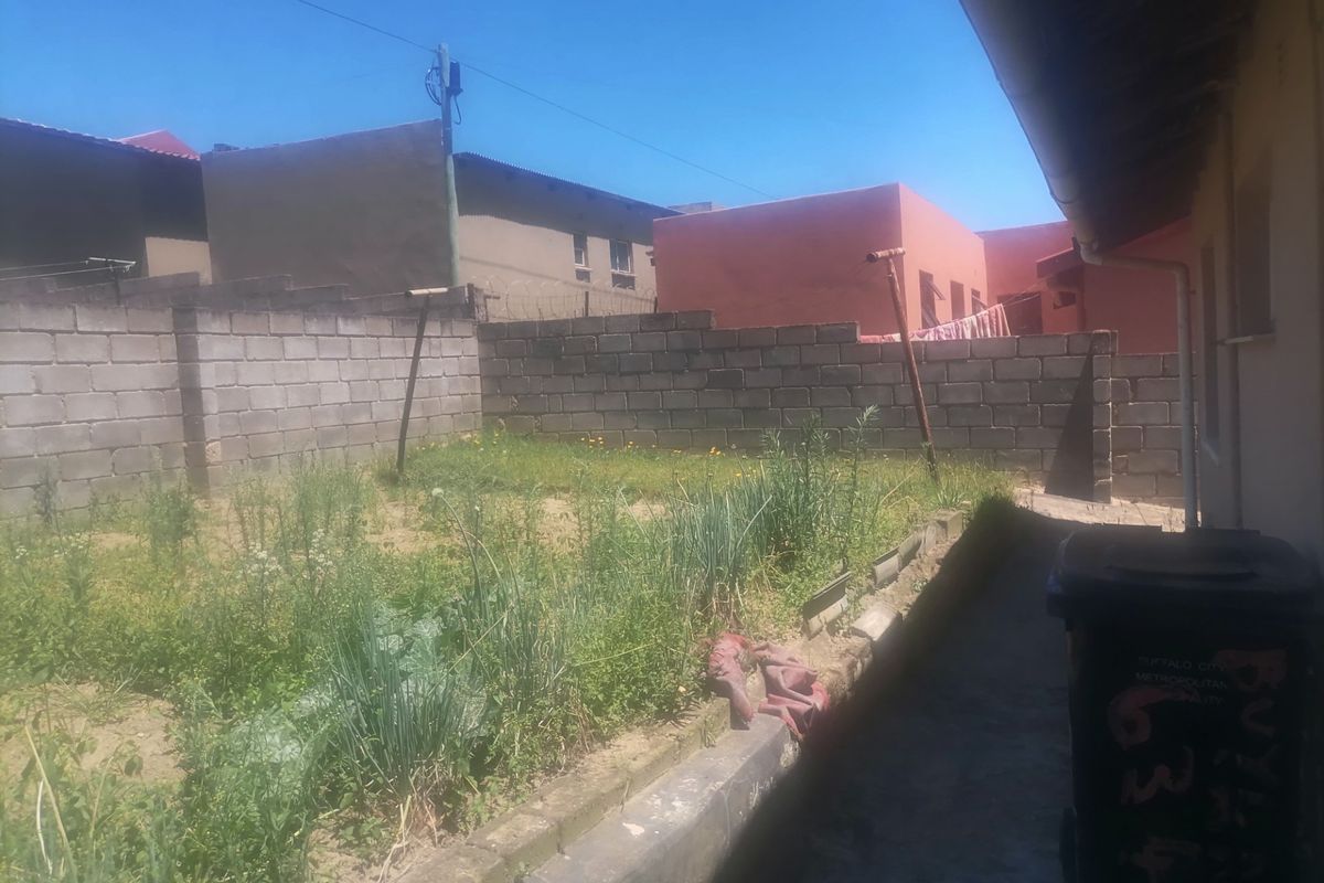 A rear exterior view of the property featuring a basic garden area enclosed by concrete block boundary walls.