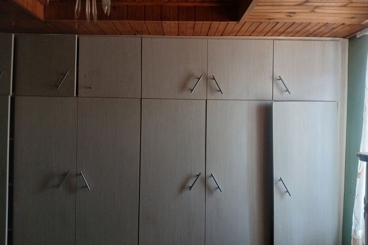 A bedroom featuring floor-to-ceiling built-in cupboards with light wood-grain finish and a timber-paneled ceiling.