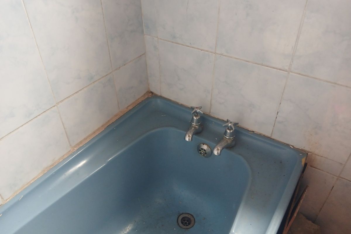 A dated bathroom featuring a blue bathtub with traditional chrome taps and light blue wall tiling.