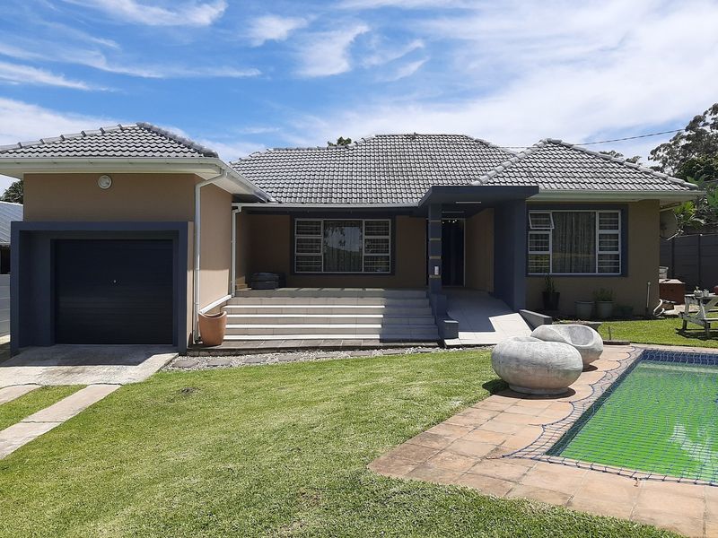 Front elevation of a single-story house featuring a tiled roof, attached garage, front entrance steps, and a swimming pool with paved surround.