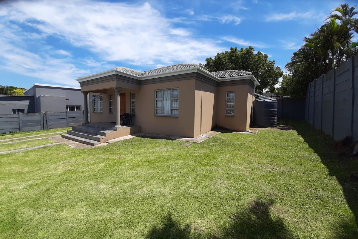 A well-maintained single-story house featuring a tiled roof, covered porch entrance, and a spacious rear garden with a water storage tank.