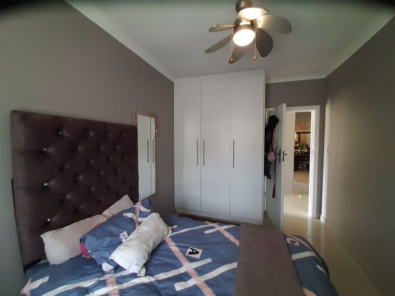 A well-maintained bedroom featuring built-in cupboards, a ceiling fan, and neutral wall finishes, with direct access to the hallway.