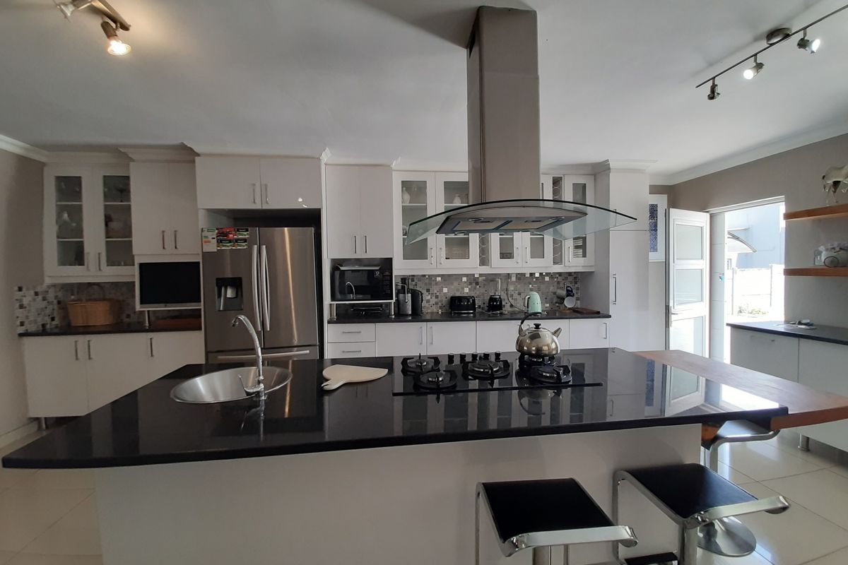 Modern kitchen featuring a large central island with granite countertops, gas hob, integrated extractor fan, and ample white cabinetry with glass-front display units.