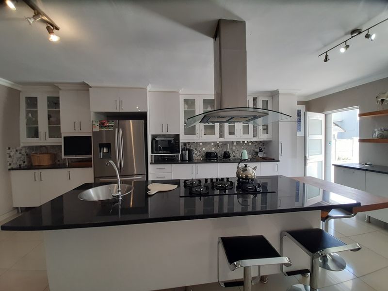 Modern kitchen featuring a large central island with granite countertops, gas hob, integrated extractor fan, and ample white cabinetry with glass-front display units.