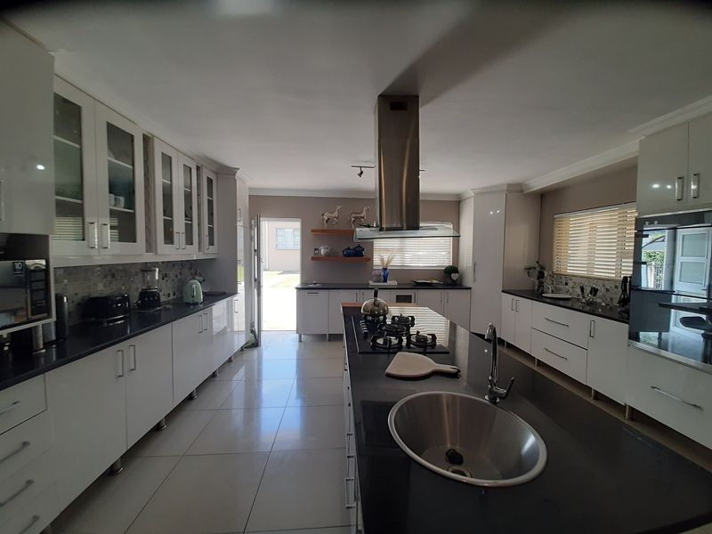 Modern kitchen featuring a central island with gas hob, sleek white cabinetry, dark countertops, and a mosaic tile backsplash with direct outdoor access.