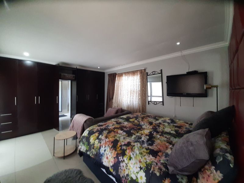 Spacious bedroom featuring extensive dark wood built-in cupboards, recessed downlighting, and neutral tiled flooring.
