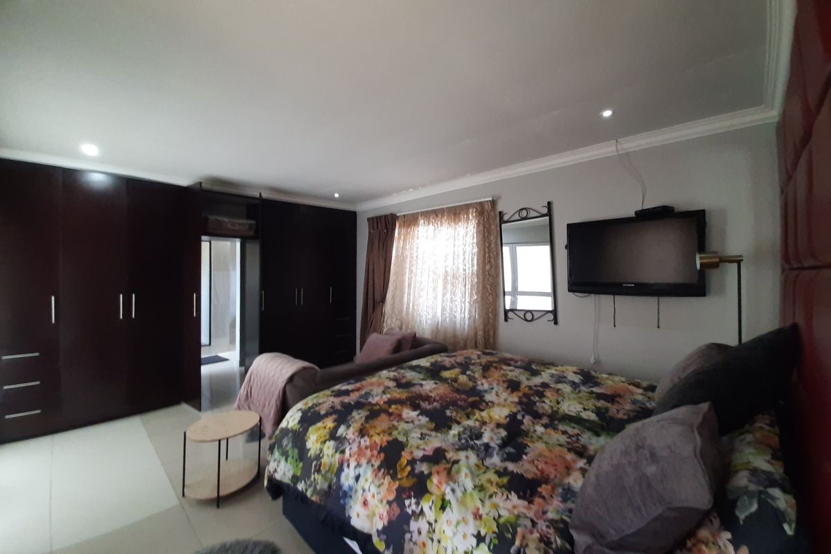 Spacious bedroom featuring extensive dark wood built-in cupboards, recessed downlighting, and neutral tiled flooring.