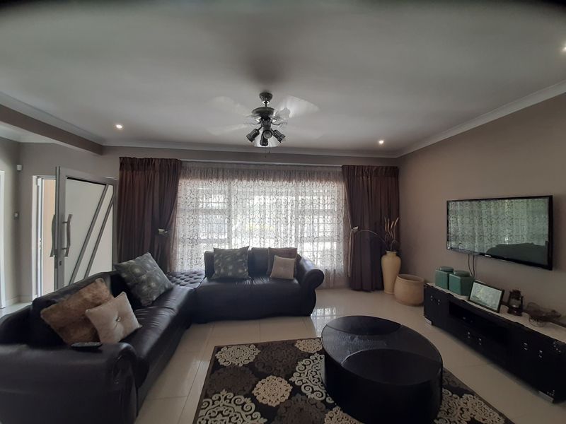 A comfortable living room featuring tiled flooring, recessed lighting, a ceiling fan, and large windows with curtains.